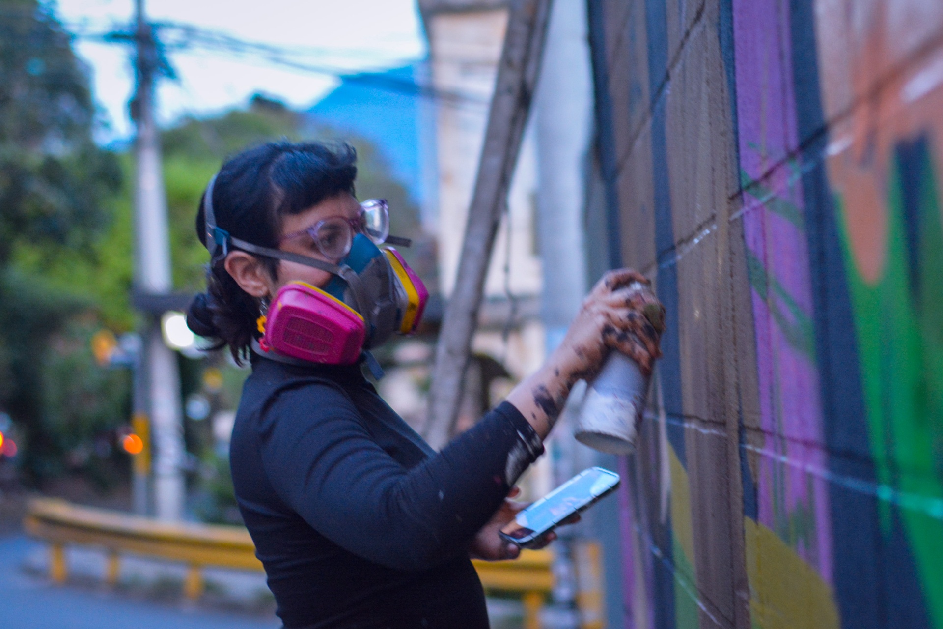 Artista con máscara antigas pintando un muro al atardecer