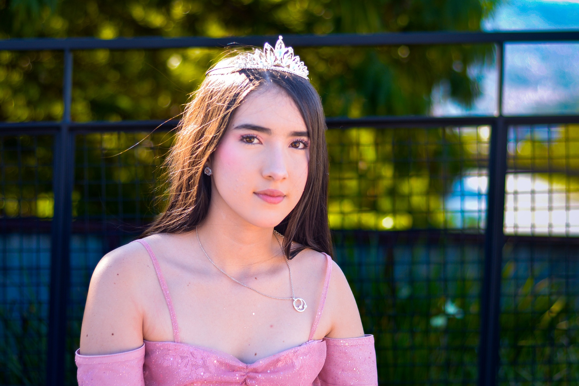 Quinceañera con corona junto a la reja, luz dorada