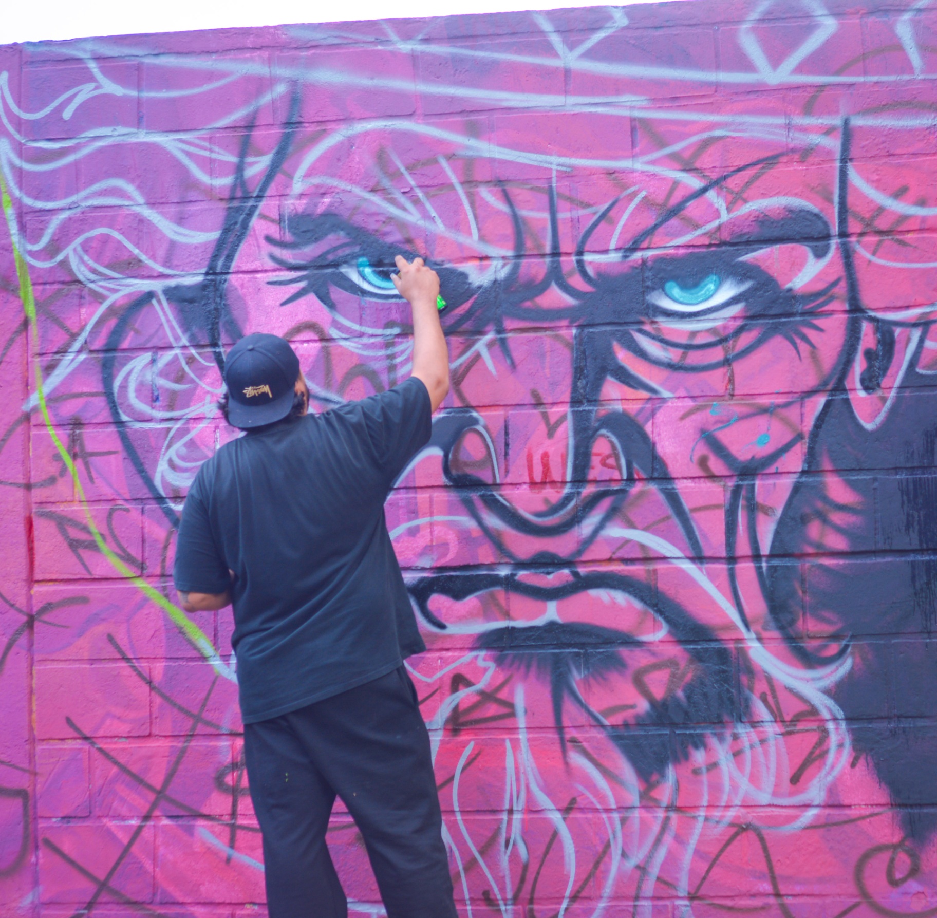 Muralista trazando ojos azules sobre fondo rosa