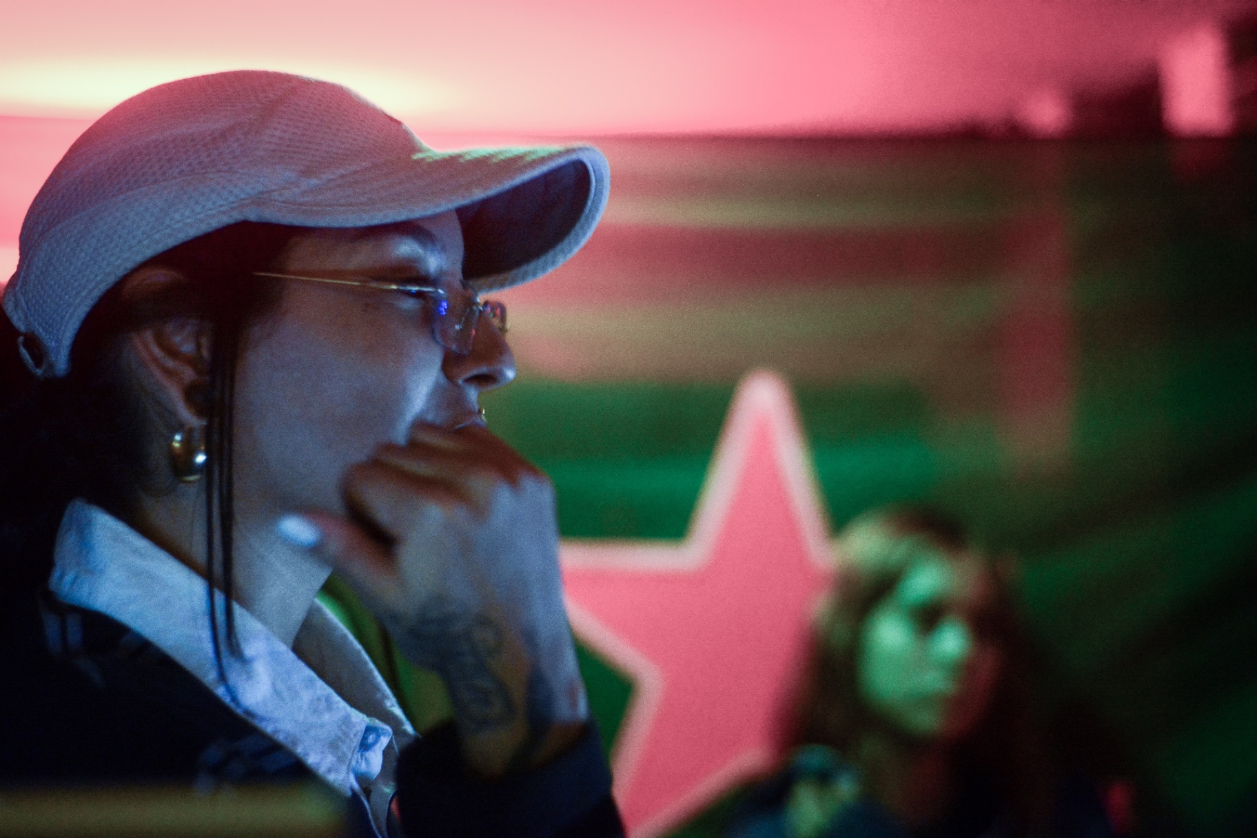 Perfil con gorra y gafas frente a pantalla rosa y verde