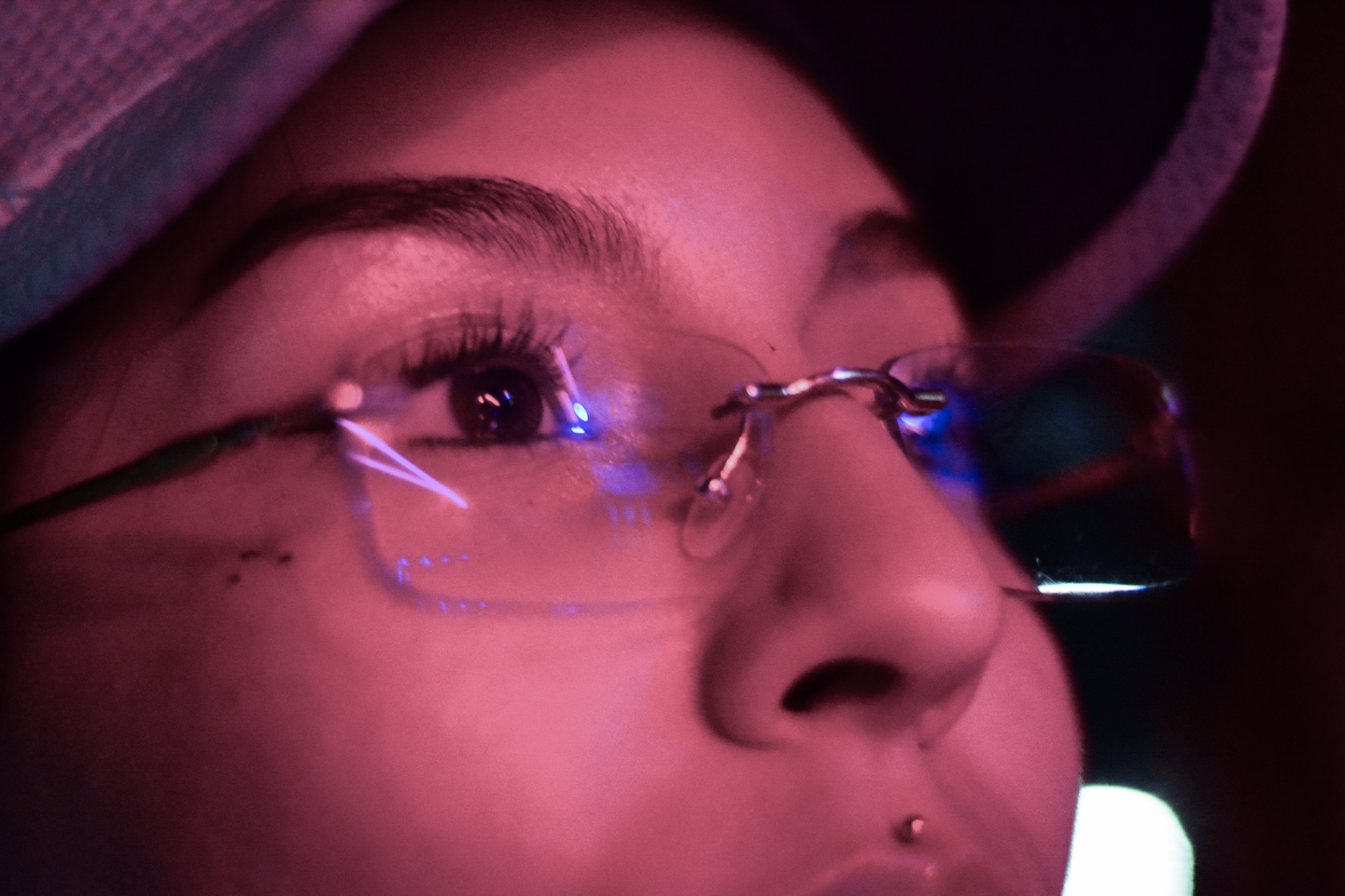 Close-up de mirada con gafas y gorra bajo luz rosada