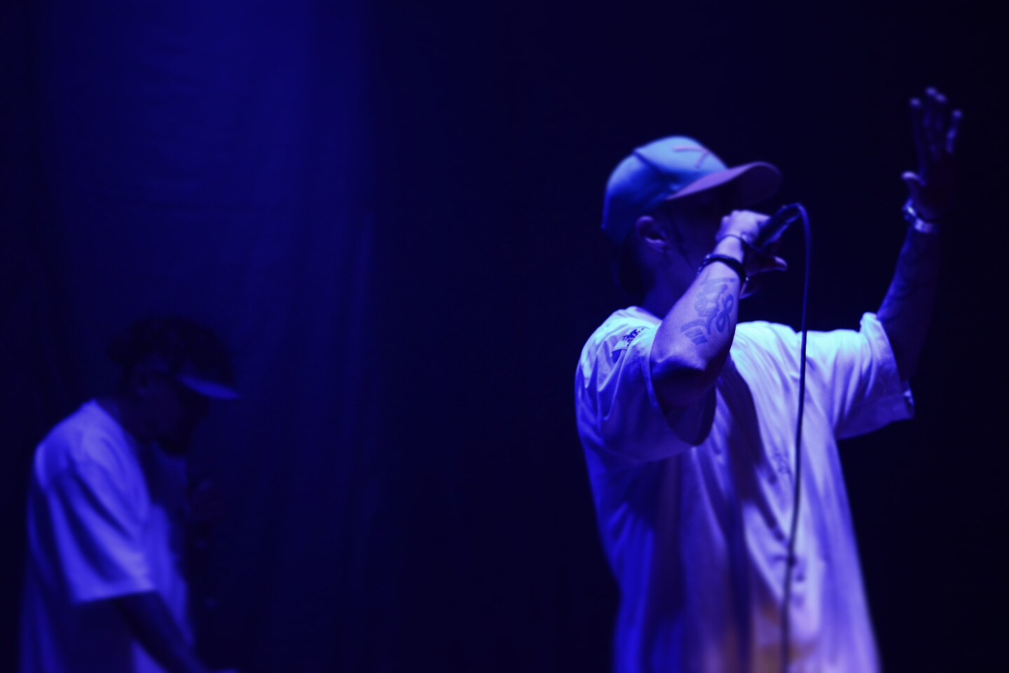 Dúo en escena bajo luz azul, productor al fondo
