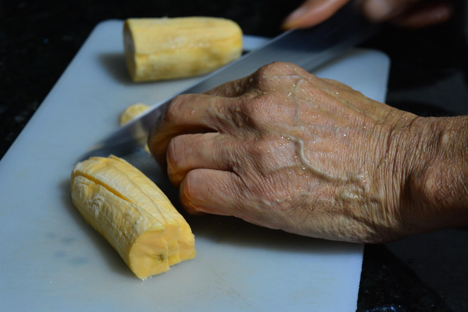Mano cortando plátano sobre tabla blanca